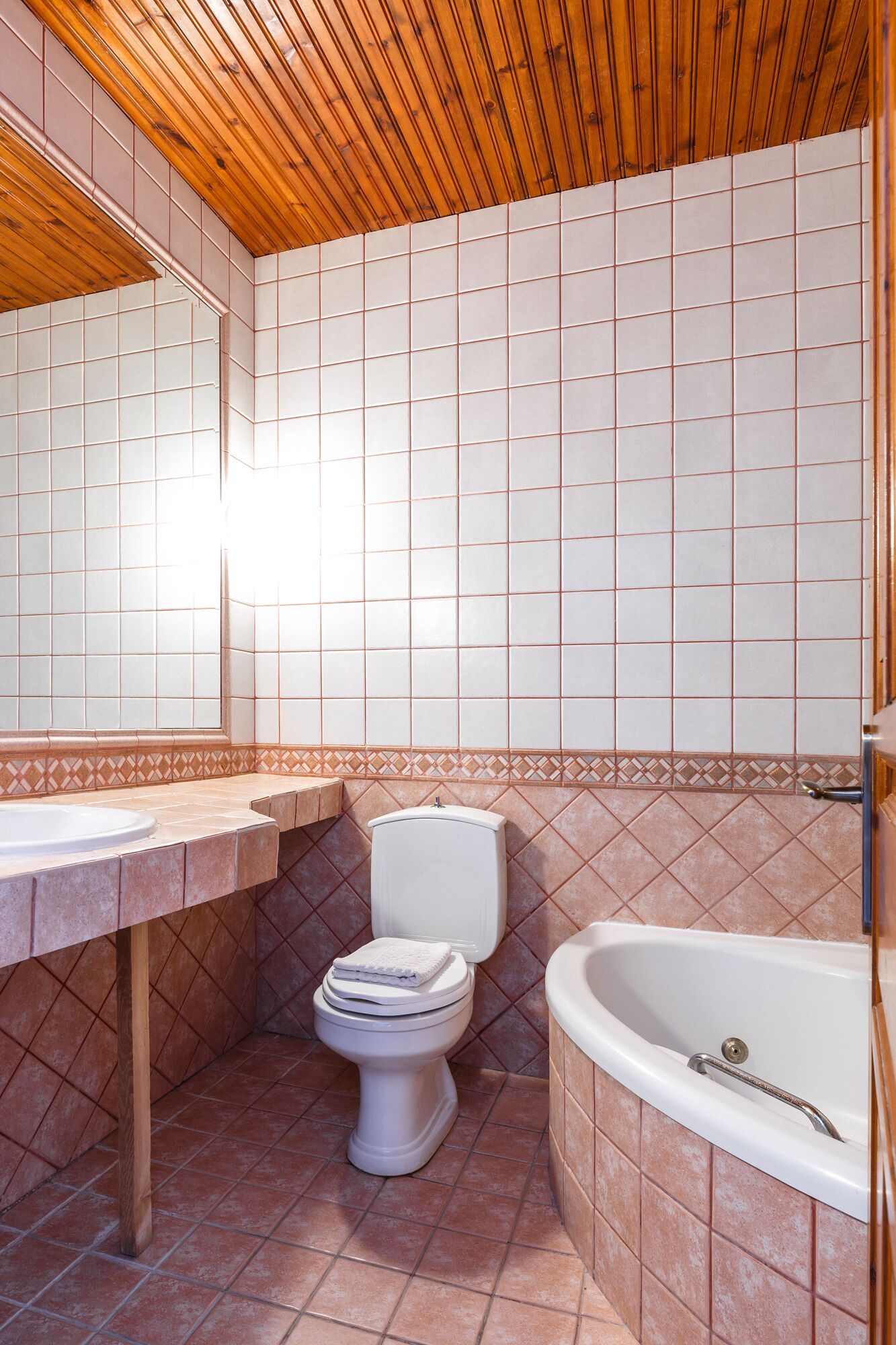 Ein Badezimmer mit Holzbalkendecke, weißen Fliesenwänden, einer weißen Toilette, einer Badewanne und einem Waschtisch.
