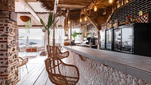 Angolo bar con sedie in vimini, parete in pietra e vista sul mare.