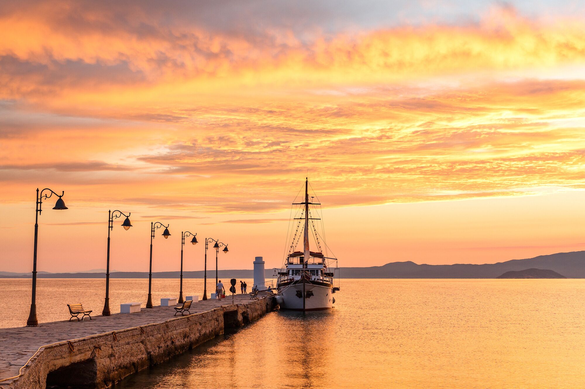 A waterfront scene with a dock, a boat, and a row of street lamps.