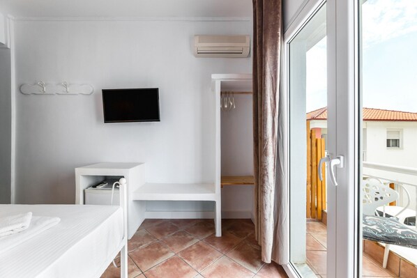 A modern, minimalist bathroom with a flat-screen TV, a white vanity, and a shower area. - Hotel Marabou (Kassandra)