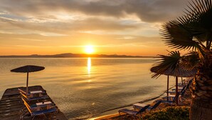 Una spiaggia con lettini e ombrelloni, un tramonto sull'acqua e palme.