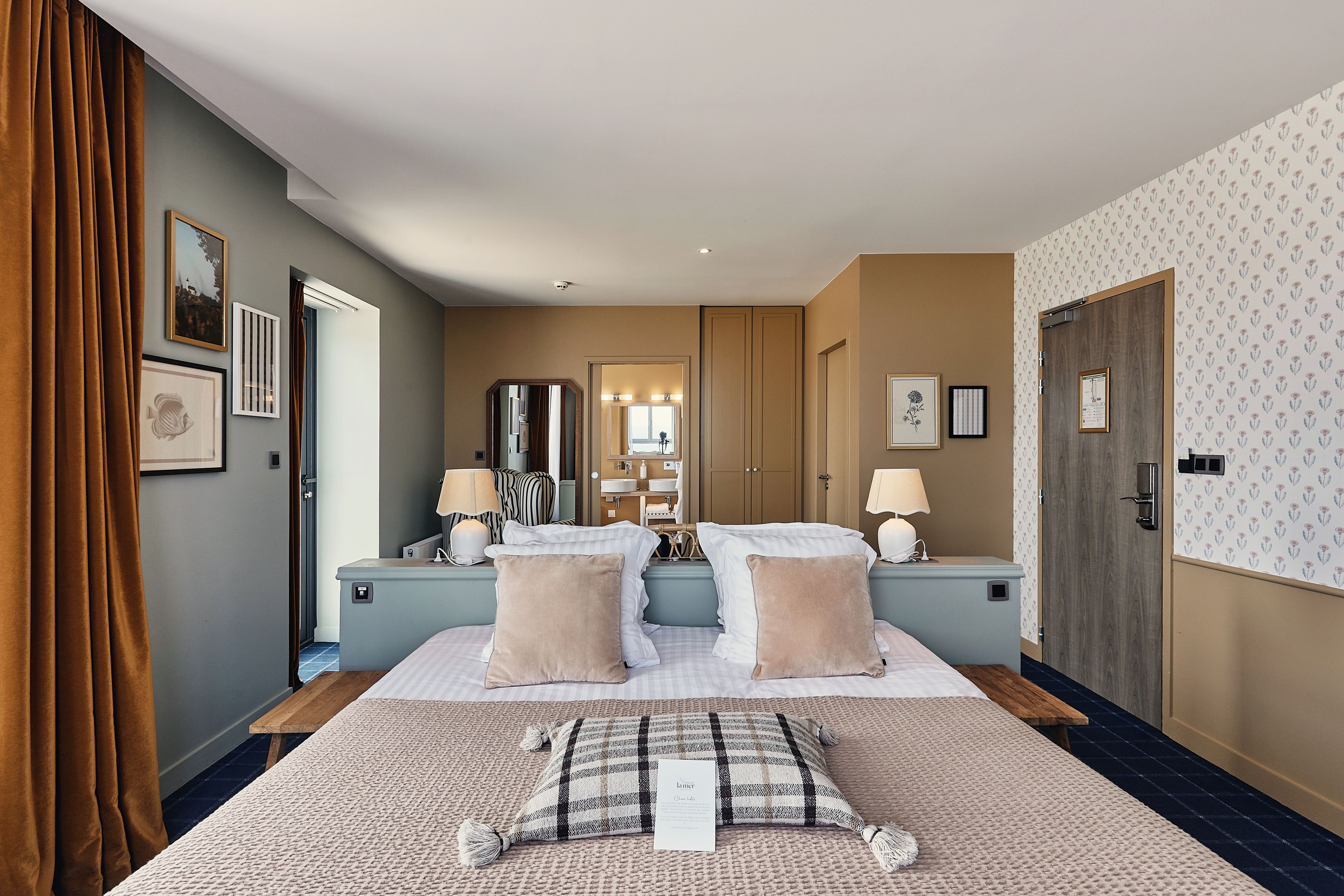 A hotel room with a large bed, bedside tables, a mirror, and a bathroom visible through an open door.