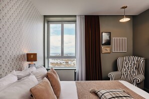 A hotel room with a bed, a chair, a window with a view of the beach, and a lamp. - Hôtel de la Mer (Plounéour-Brignogan-Plages)