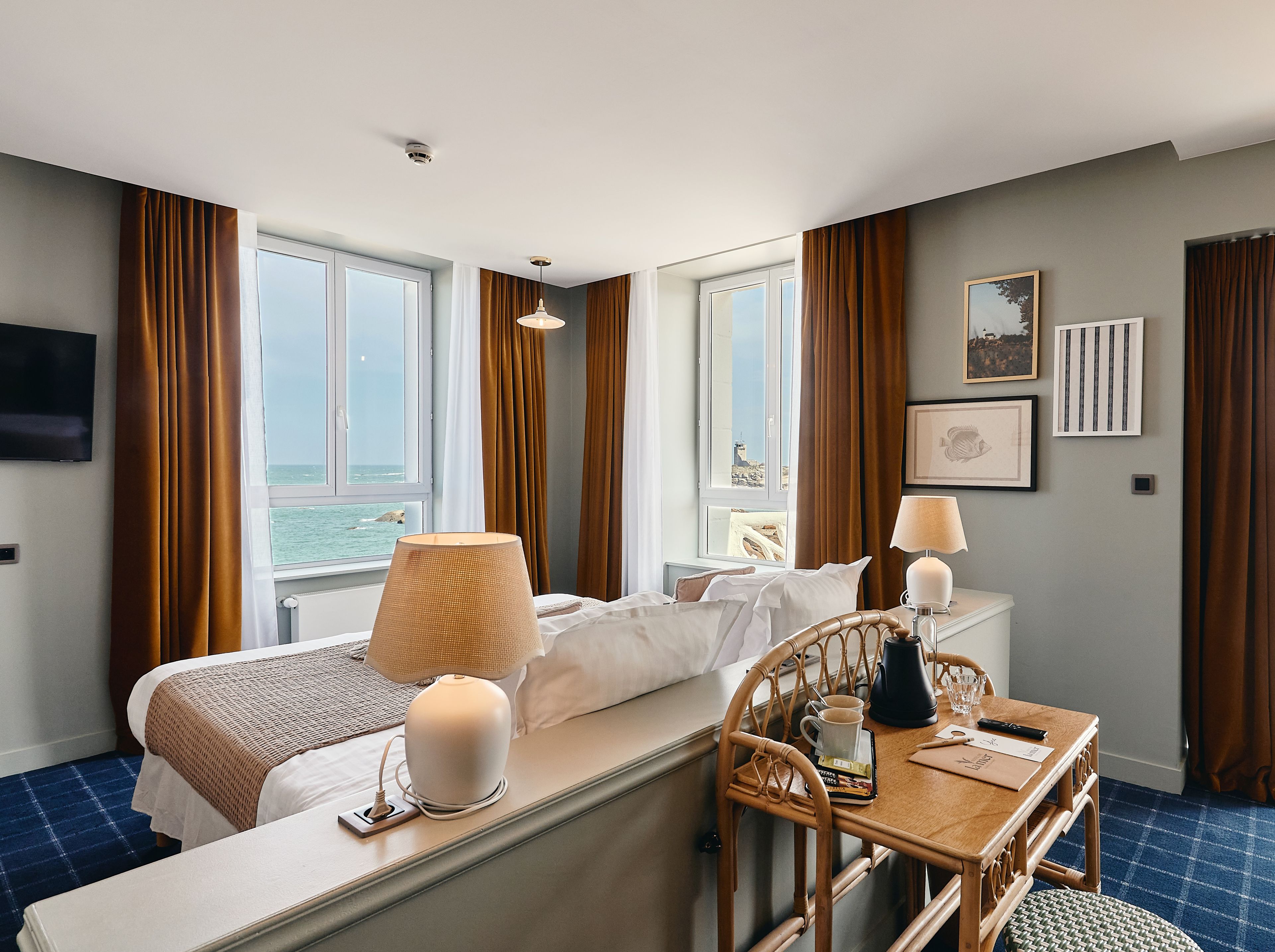 Habitación de hotel con cama, mesita de noche, lámpara y vista al mar.