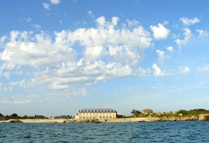 A coastal building with multiple windows, situated near a rocky shoreline and a body of water. - Hôtel de la Mer (Plounéour-Brignogan-Plages)