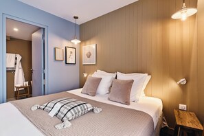 Un dormitorio con cama, mesita de noche, lámpara de pared y puerta que da al baño.