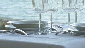 A table set with clear glasses and plates, overlooking the sea.