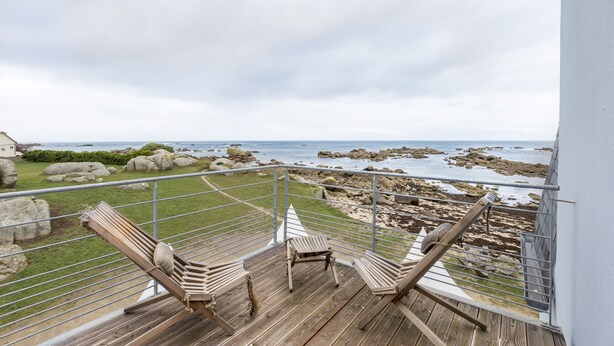 A balcony with wooden chairs and a view of the rocky coastline.
