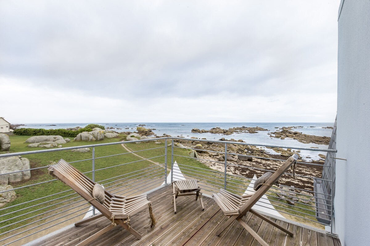Un balcón con sillas de madera y vistas a la costa rocosa.