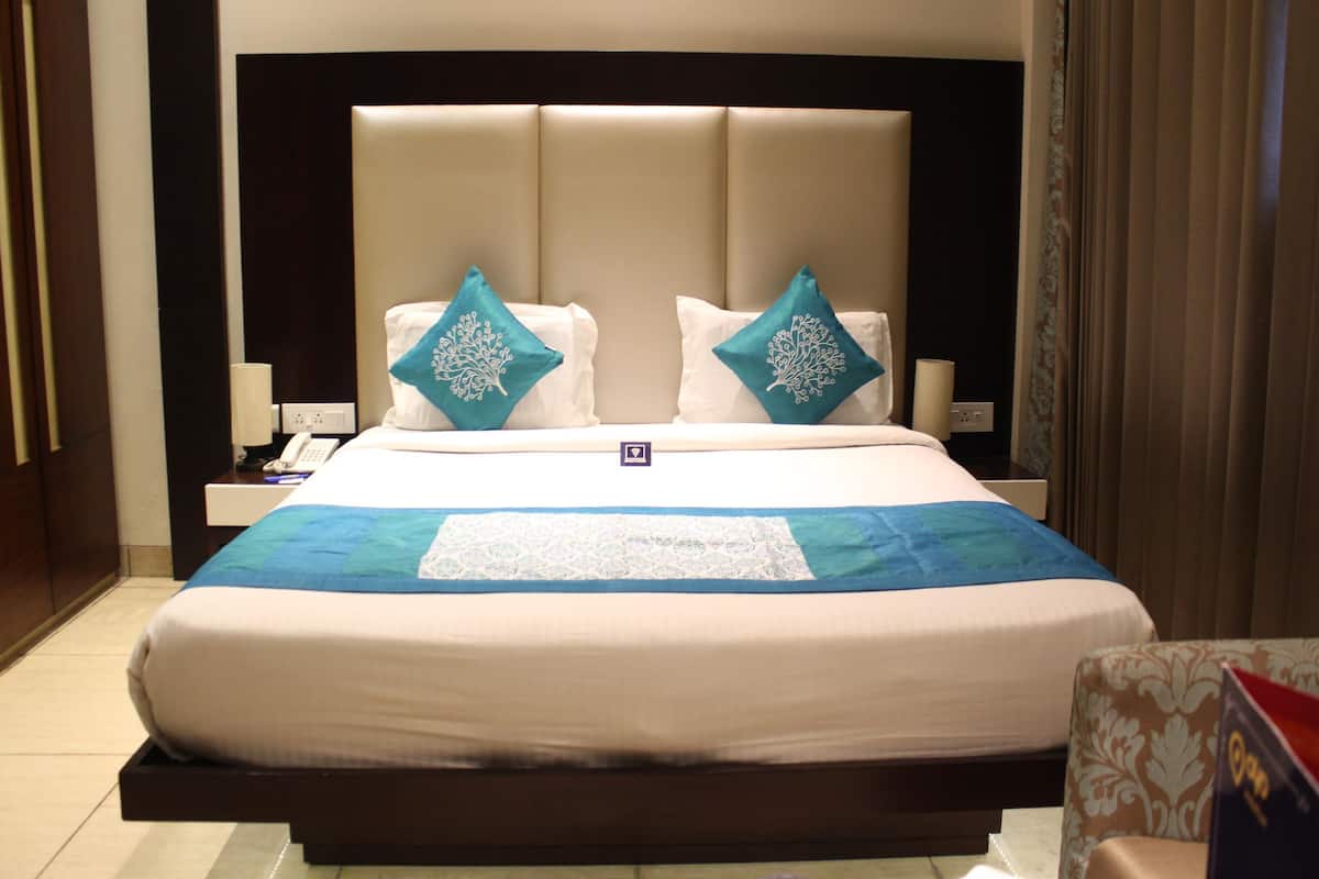 Una habitación de hotel con una cama grande, dos almohadones decorativos, una mesita de noche con lámpara y un teléfono.