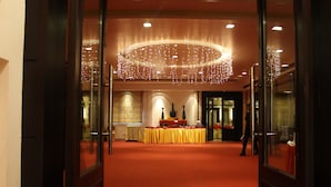 Un vestíbulo de hotel con alfombra roja, una recepción con mantel amarillo y una gran lámpara de araña circular.