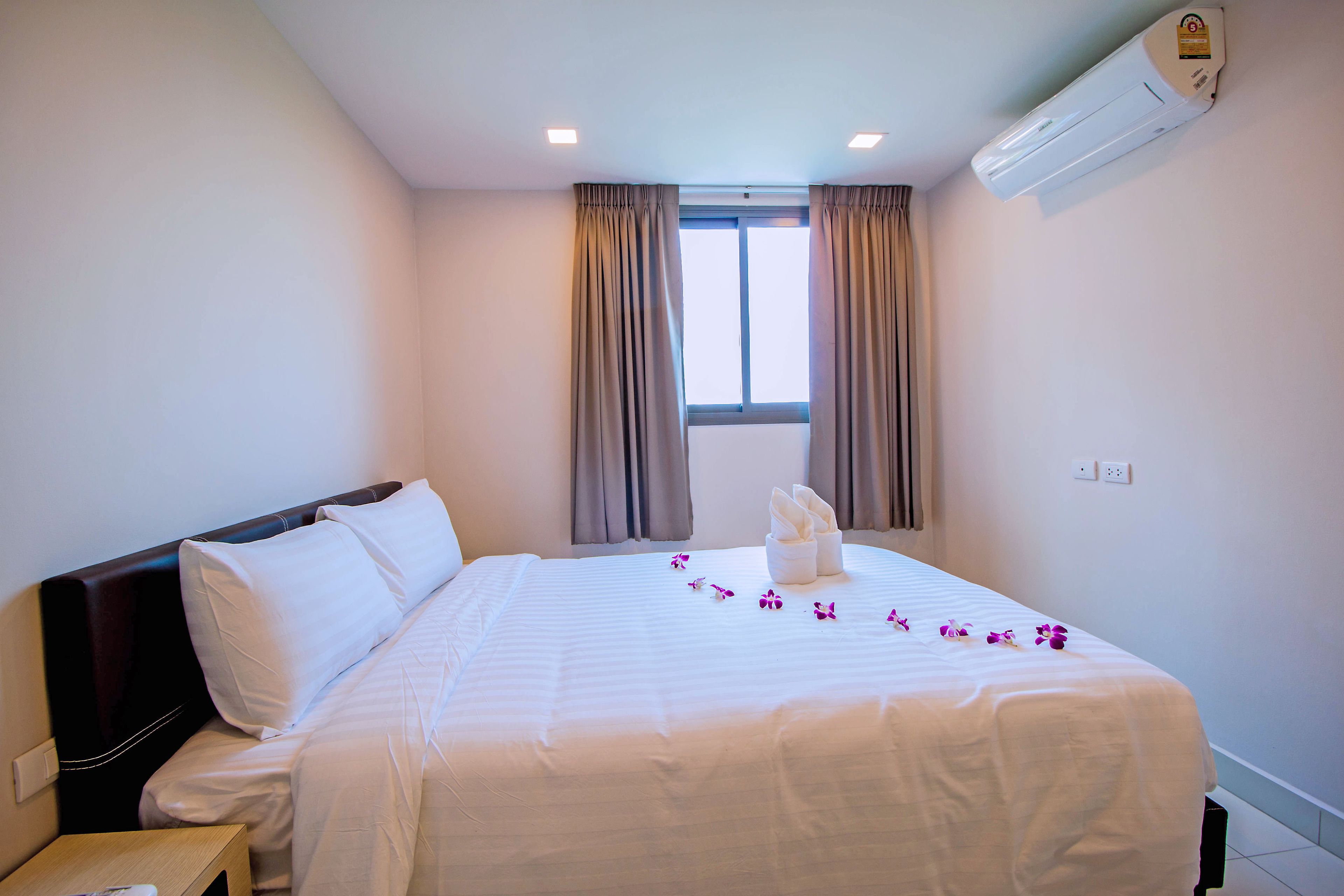 Une chambre d’hôtel avec un grand lit, une table de chevet, un appareil de climatisation et une fenêtre avec des rideaux.