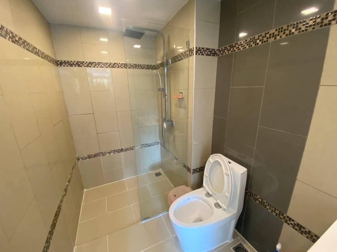Egy fürdőszoba zuhanyzóval, WC-vel és csempézett falakkal.