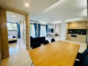 Quarto de hotel moderno com uma mesa de jantar de madeira, um sofá e uma área de cozinha com armários e uma televisão.