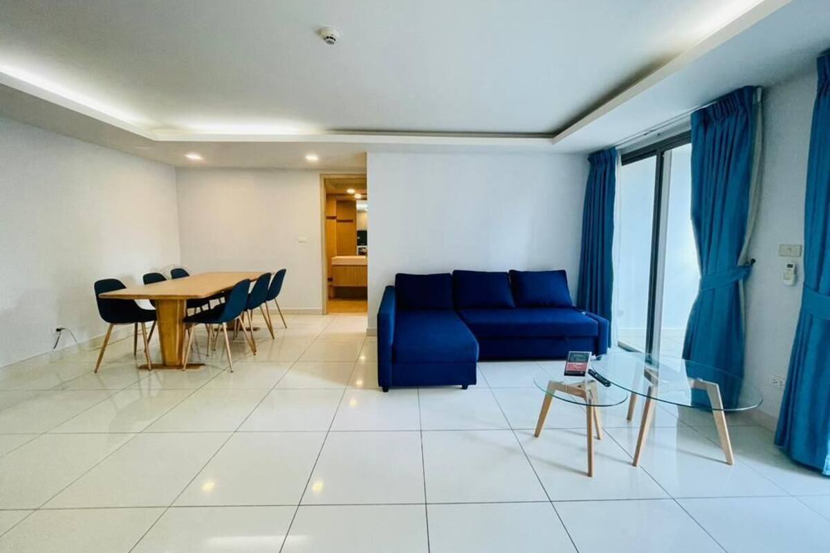 A modern living room with a blue sofa, a wooden dining table with chairs, and a glass coffee table.