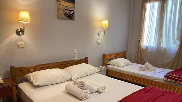 Et hotelværelse med to senge, et træsengegærde, en vægmonteret lampe og et vindue med gardiner.
