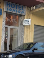 Un hotel llamado "HOTEL IONION" con fachada de mármol y una persiana baja.