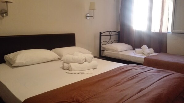 Habitación de hotel con dos camas, cada una con sábanas y almohadas blancas, una mesita de noche, una lámpara de pared y un ventanal con cortinas.