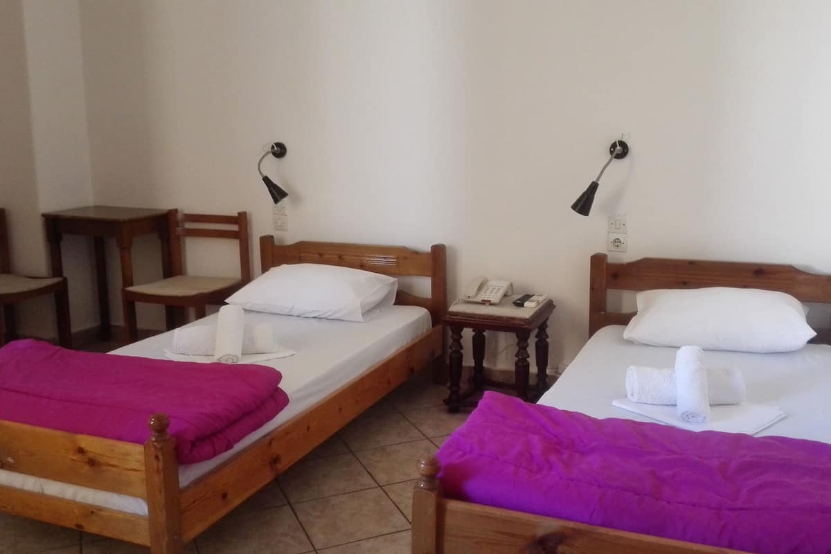 Dos camas de madera con sábanas blancas y mantas moradas, una silla de madera, una mesita de madera y un teléfono instalado en la pared.