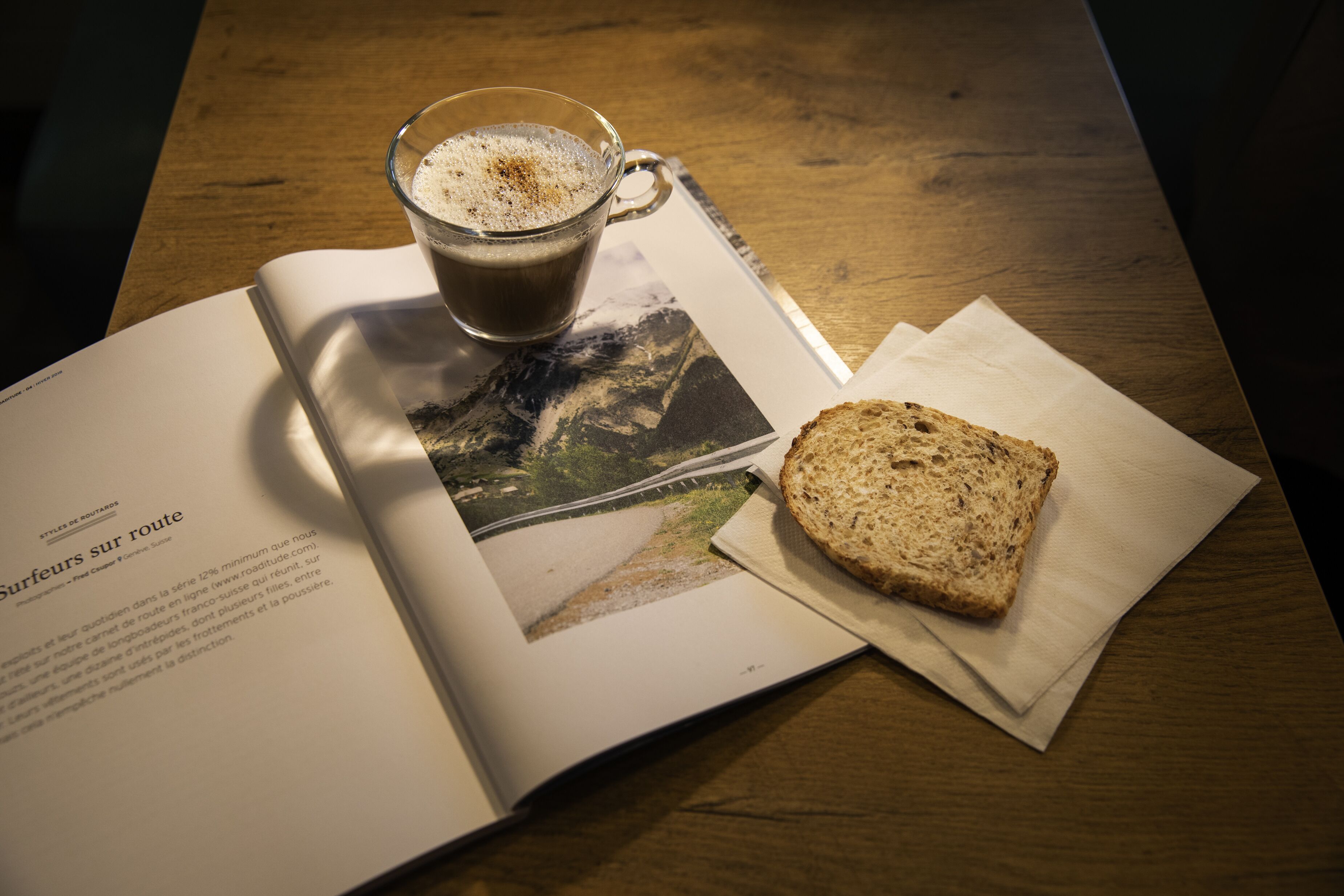 A book open on a wooden table with a cup of coffee, a slice of bread, and a photograph.