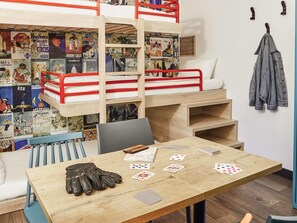Una cama litera con carteles, una mesa con cartas, una chaqueta y una silla.