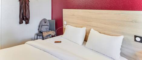 Una habitación de hotel con cama, escritorio, silla y perchero.
