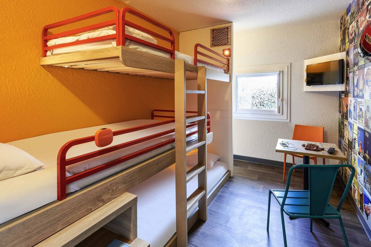 A bunk bed room with a desk and chair, a TV, and a window.