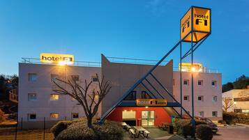 Een hotel met een opvallend 'hotel F1' bord, een rode ingang en een parkeerplaats met picknicktafels.