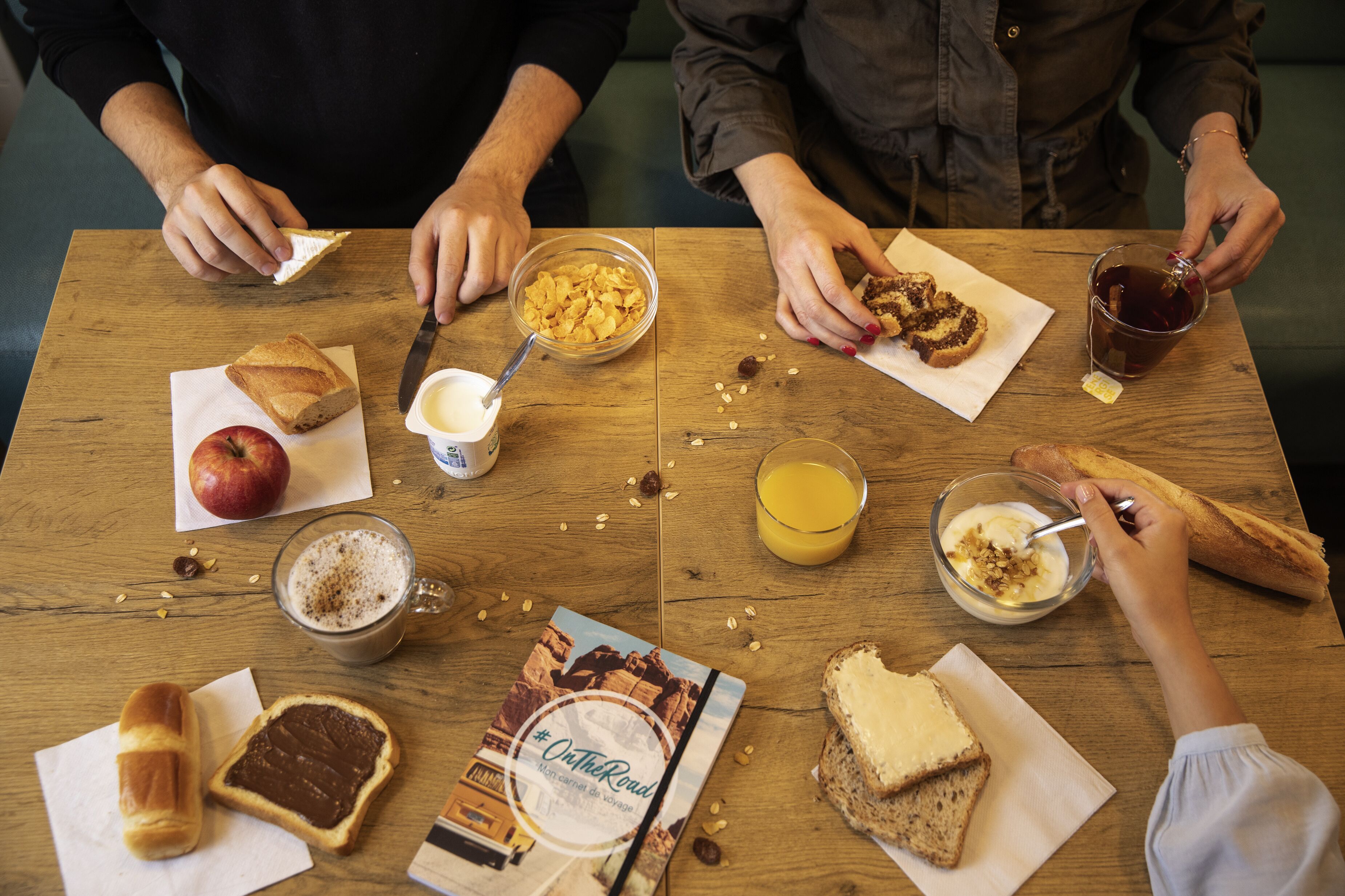 A wooden table with various breakfast items including bread, an apple, cereal, coffee, and a book titled "On the Road".