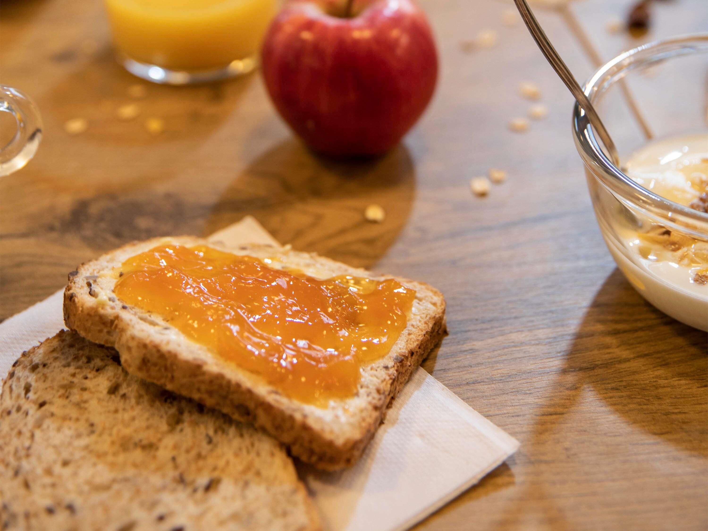 Une table mise pour le petit-déjeuner avec des tartines, de la confiture, une pomme et un bol de céréales.