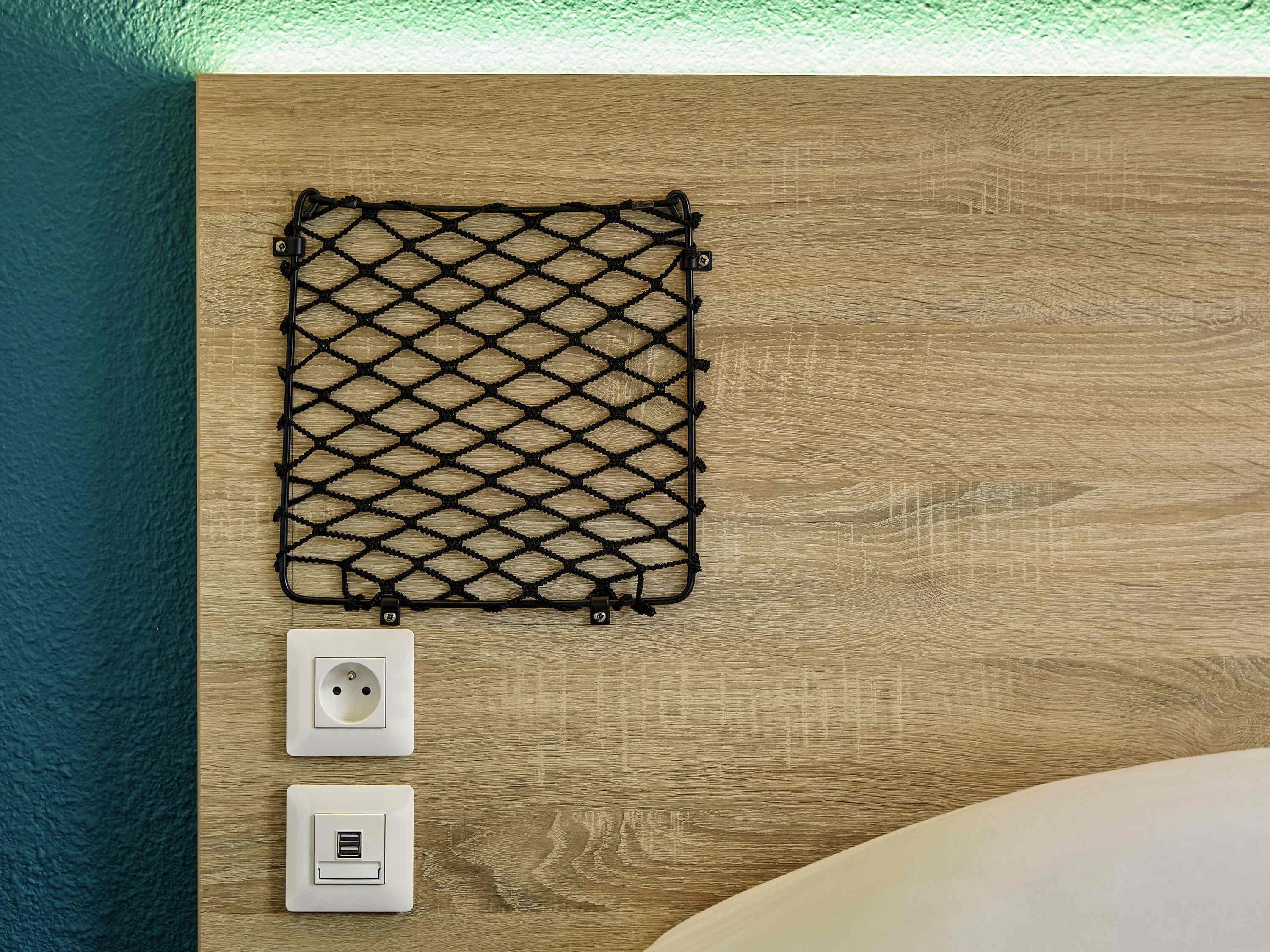 A wooden wall with a black mesh shelf, two electrical outlets, and a white switch.