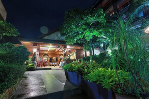 A well-lit hotel entrance with a covered outdoor seating area, surrounded by lush greenery and potted plants. - Baan Vanida Garden Resort (Karon)
