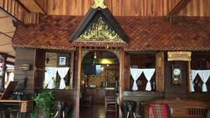 Un edificio de madera tradicional con un arco central, un letrero que indica un restaurante y estatuas de elefantes.