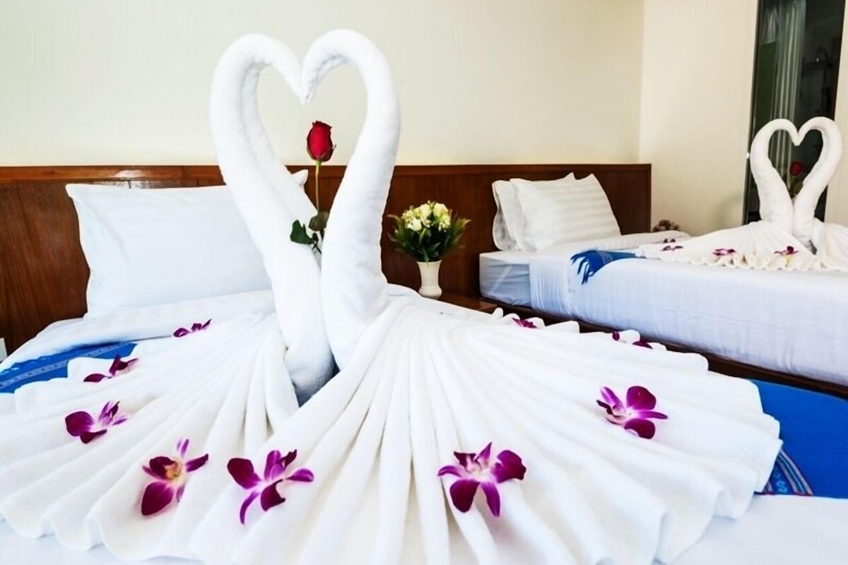 A hotel room with two beds, each adorned with white towels arranged in a heart shape and purple orchids.