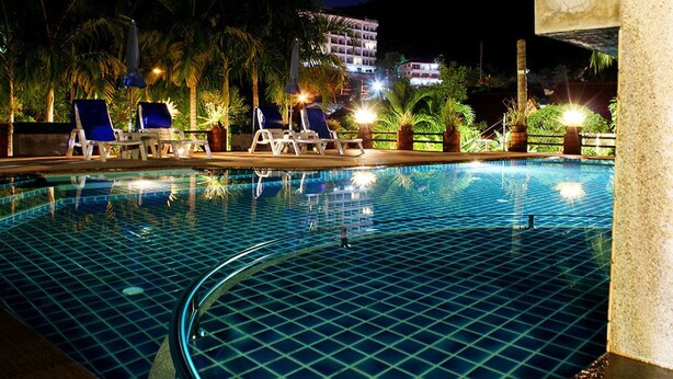 Una piscina con sillones de descanso y palmeras de noche.
