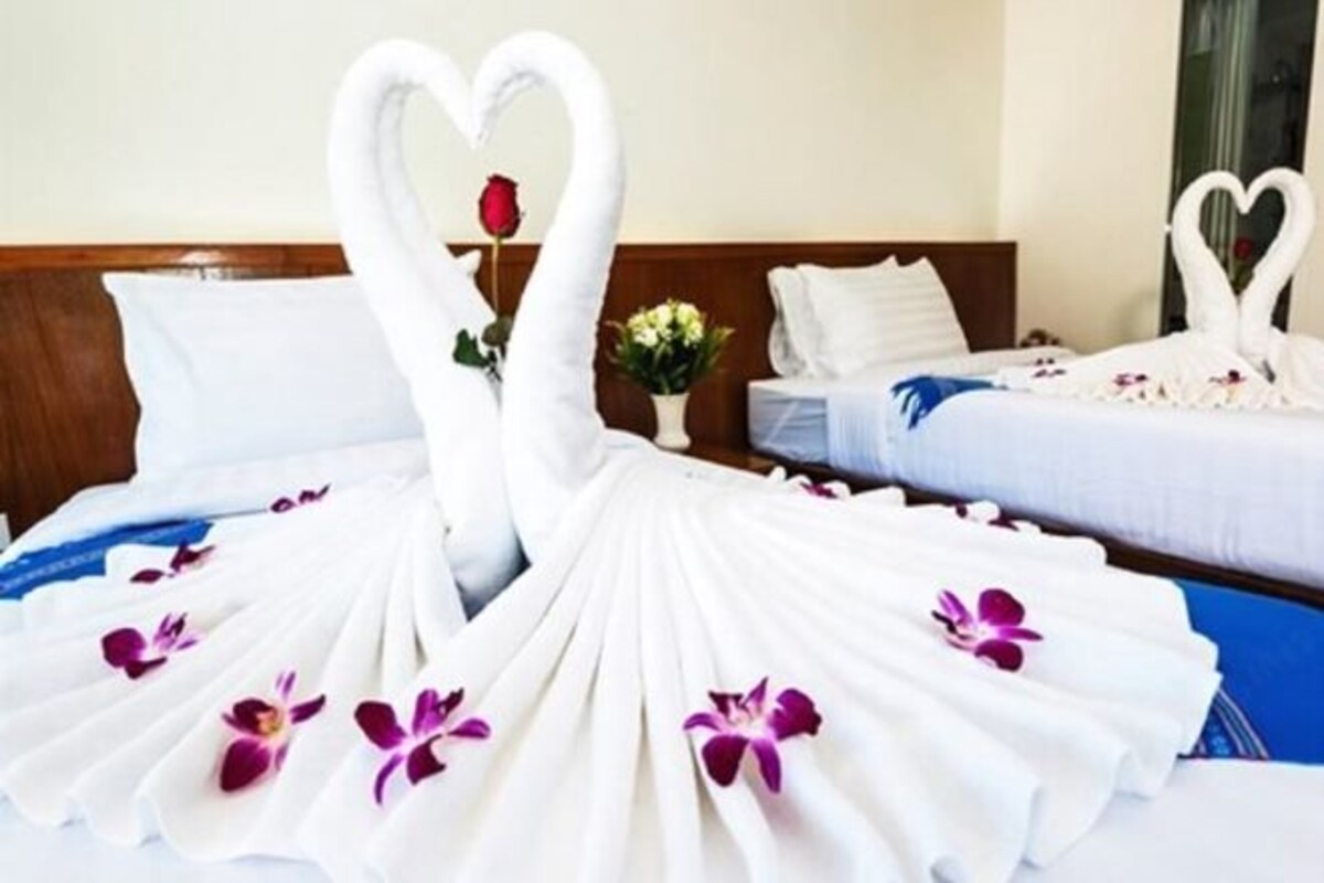 A hotel room with two beds, one with a heart-shaped towel arrangement and the other with a swan-shaped towel arrangement.