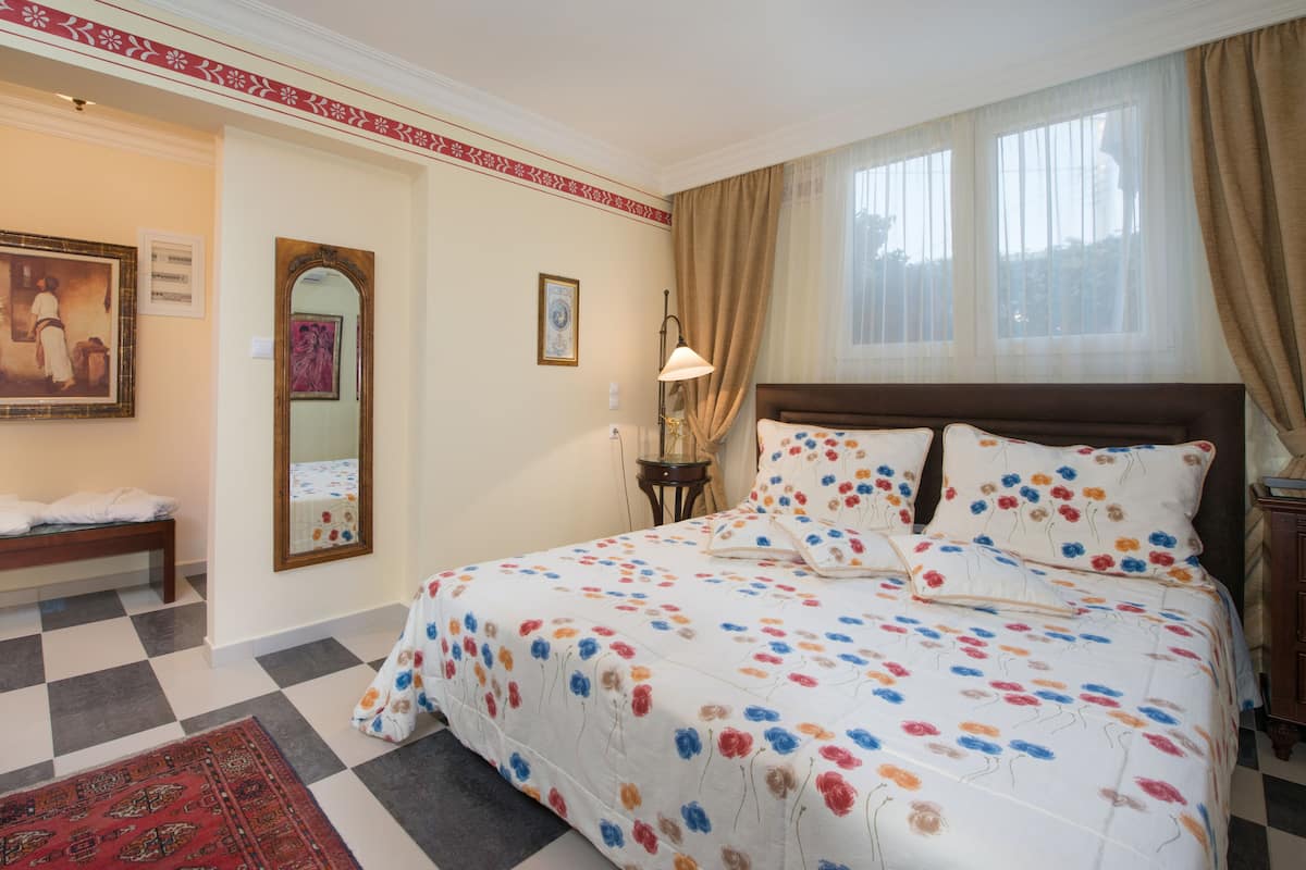Une chambre d’hôtel avec un grand lit, un banc, un miroir et une fenêtre avec des rideaux.