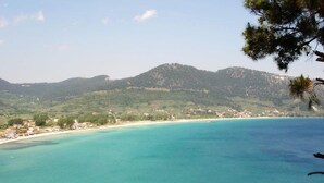 Un paysage côtier avec une plage, des eaux turquoise et limpides, et une ville en arrière-plan.