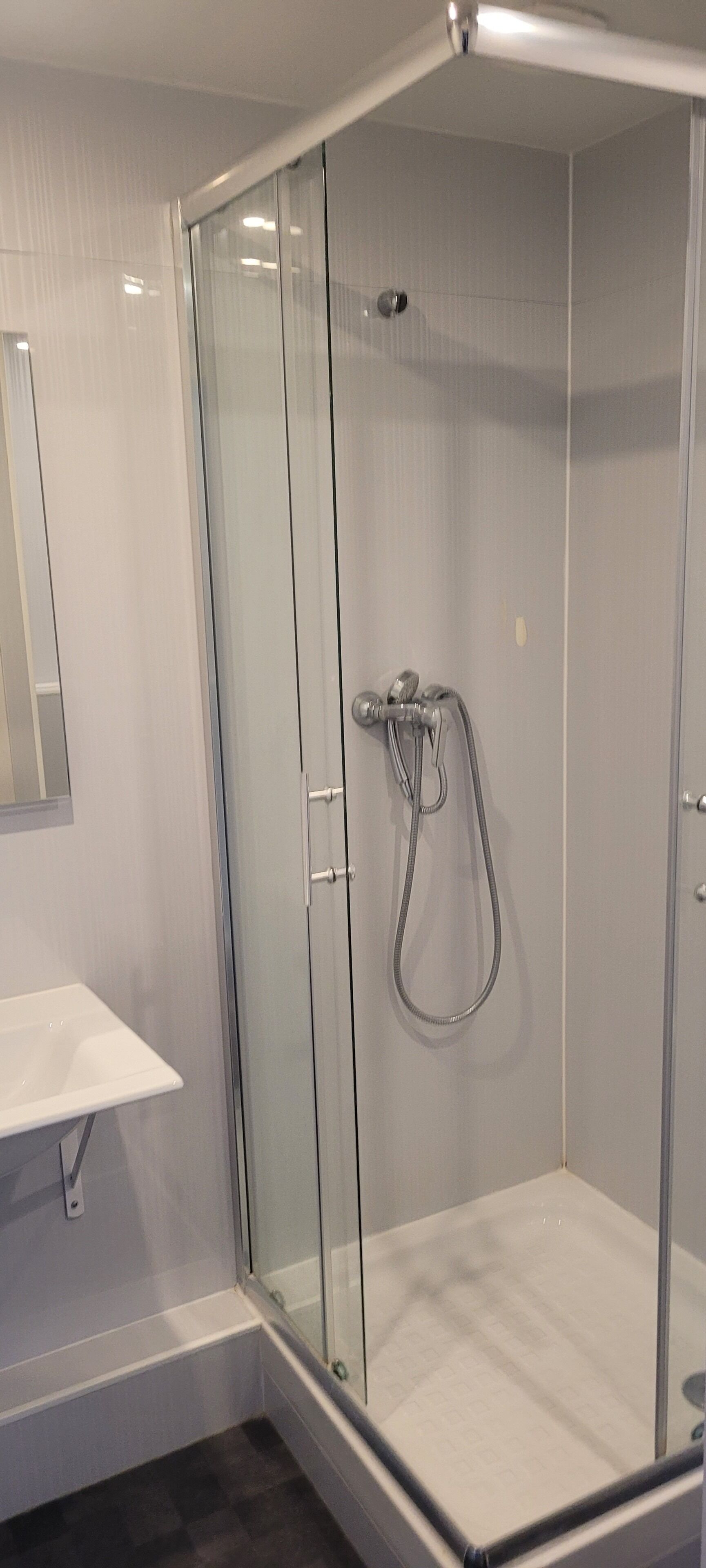 Une salle de bain moderne avec une douche à parois de verre, un lavabo blanc et un miroir au mur.