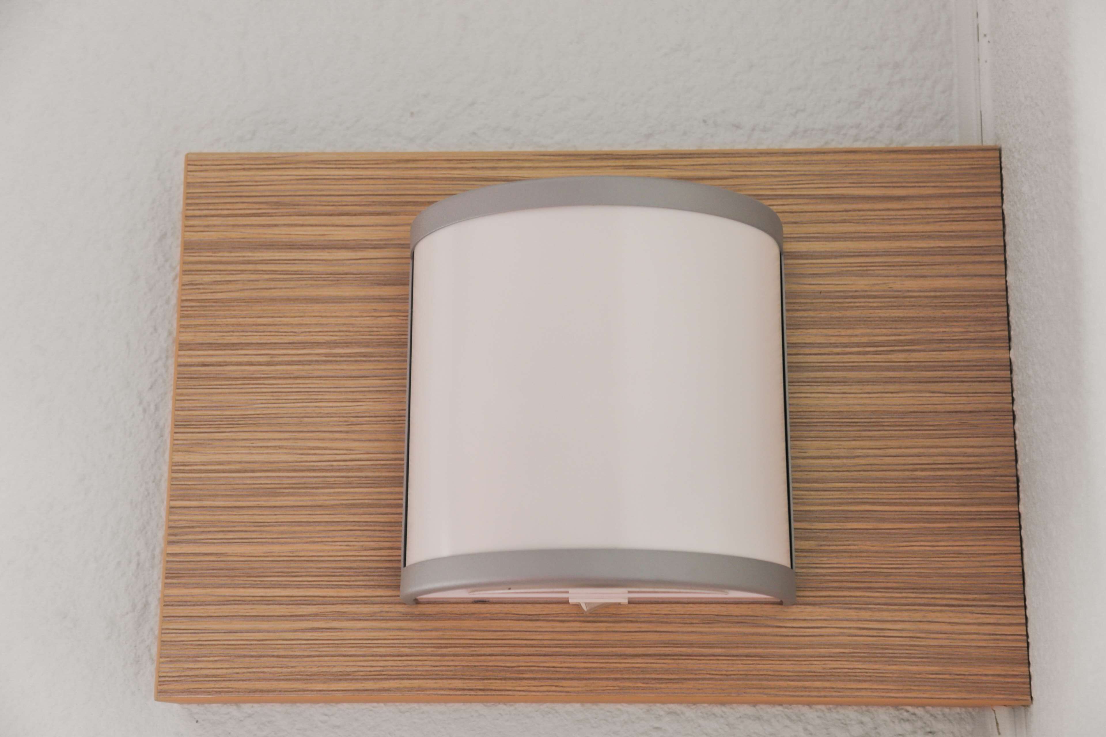 Una lámpara de pared con forma cilíndrica y detalles metálicos, instalada en un marco de panel de madera.