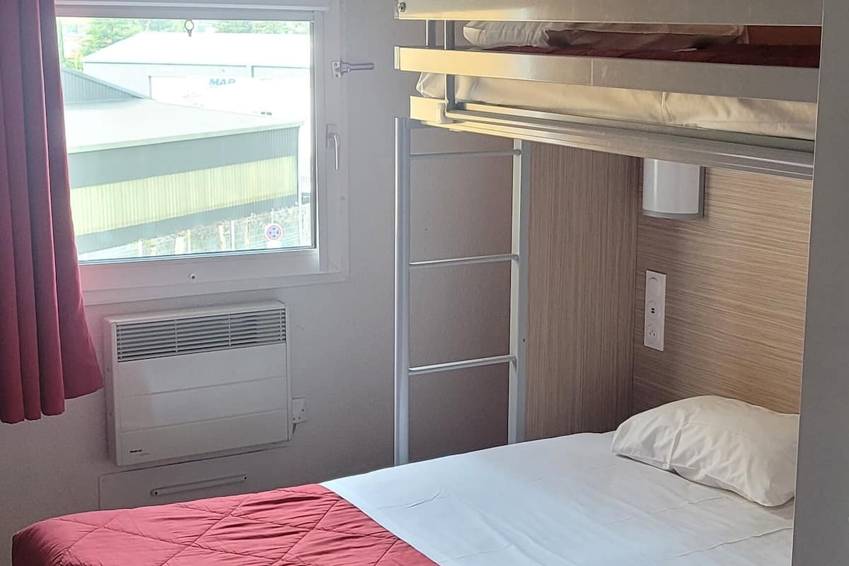 A bunk bed with a red mattress, a window with curtains, and a radiator.