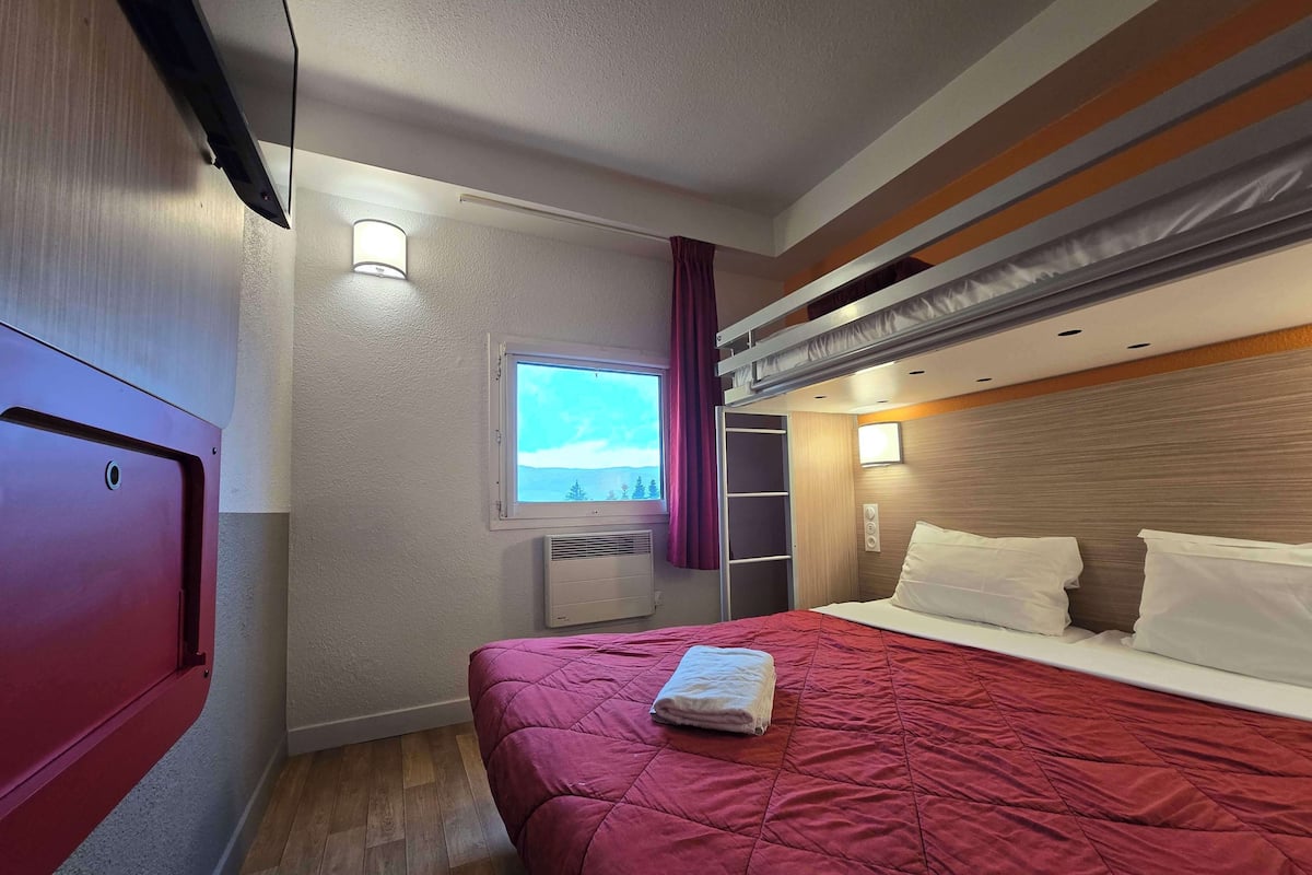 A hotel room with a bunk bed, a window with a view, a heater, and a wardrobe.