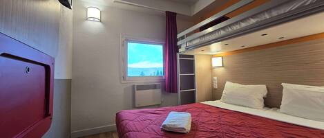 A hotel room with a bunk bed, a window with a view, a heater, and a wardrobe.