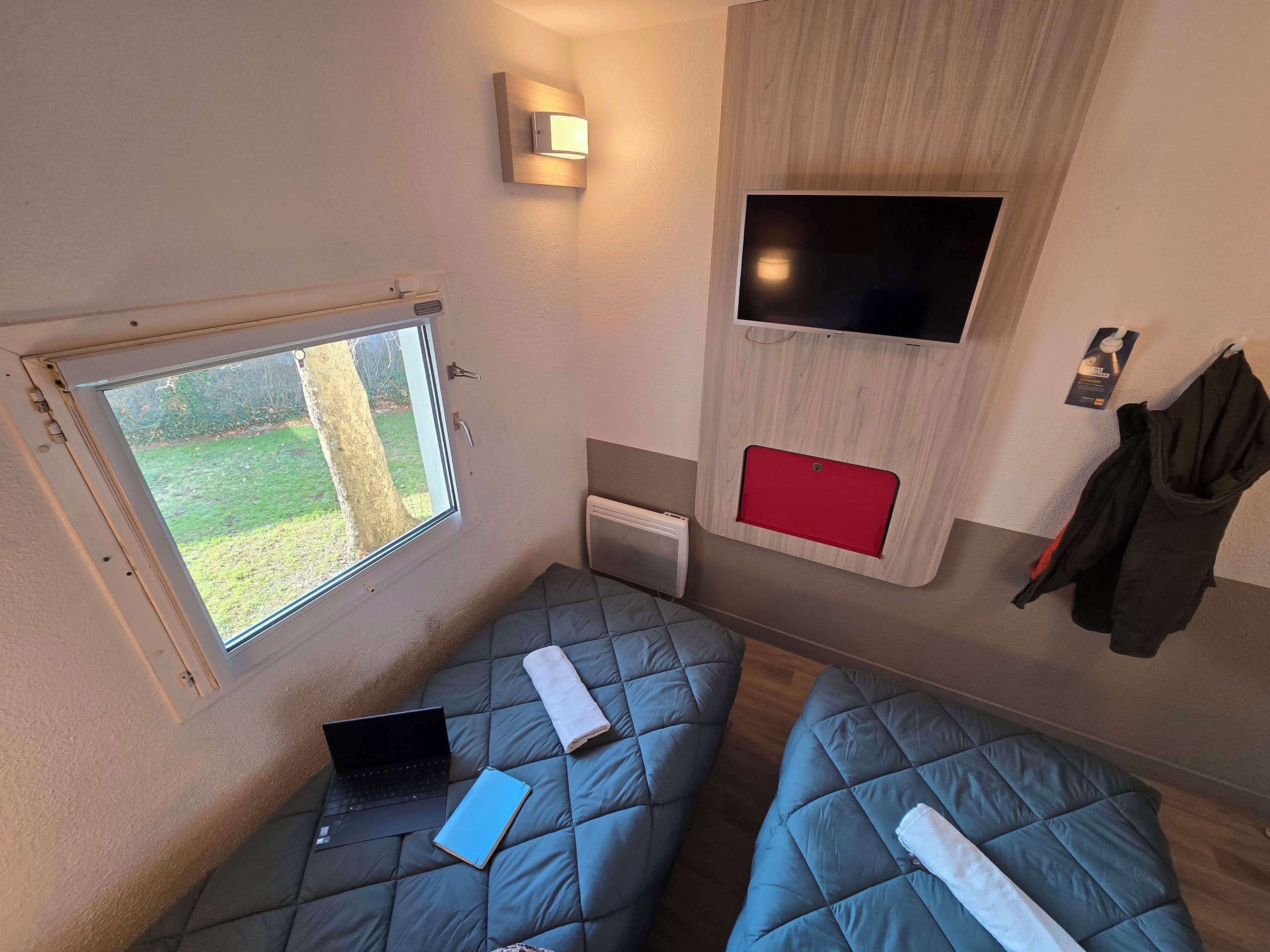 A compact room with two beds, a laptop, a notebook, and a TV mounted on the wall.