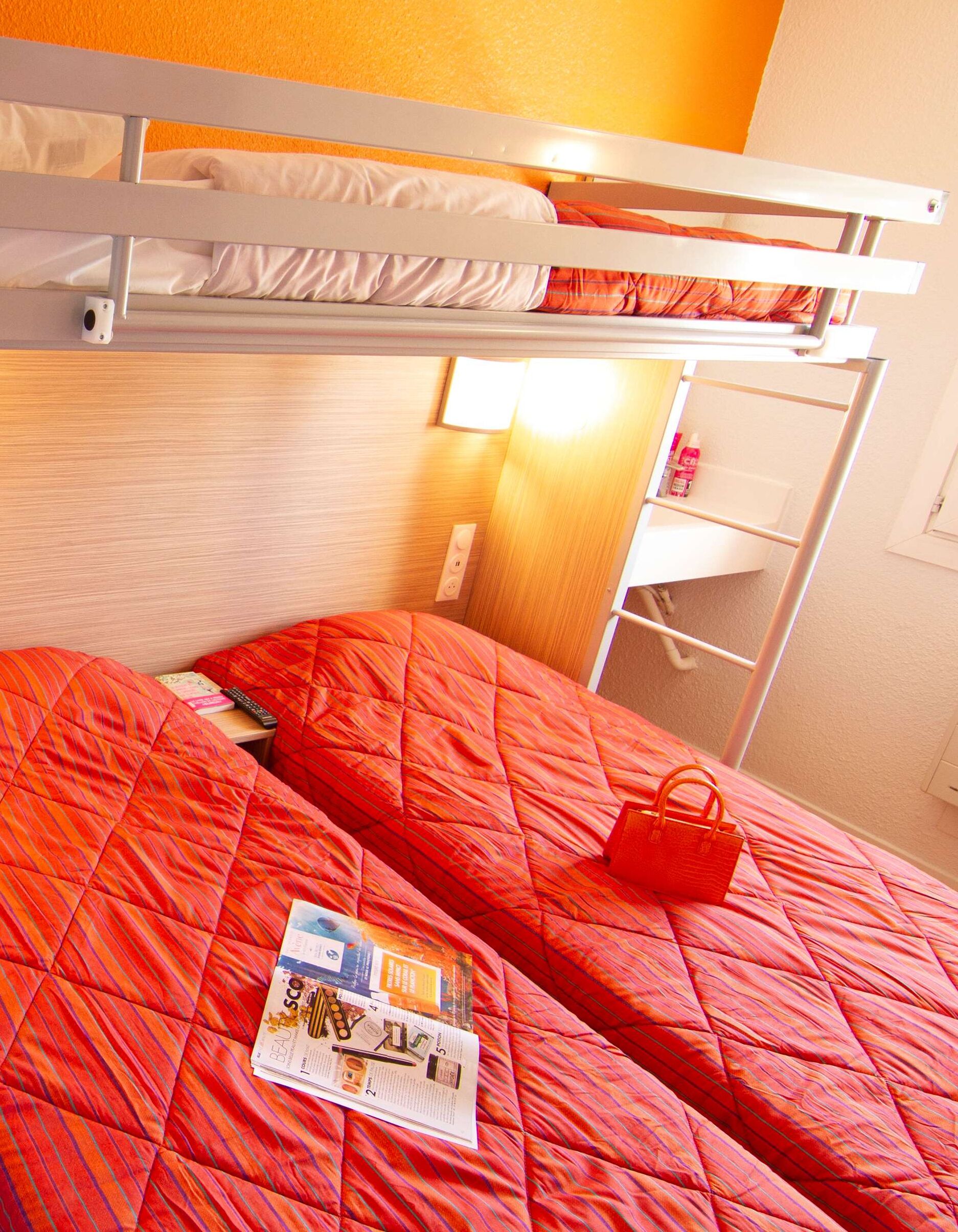 A bunk bed with a red quilted bedspread and a magazine on the lower bunk.