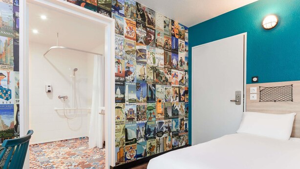 A hotel room with a bed, a shower, a wall covered with travel posters, and a blue accent wall. - hotelF1 Lyon Gerland Vénissieux (Venissieux)