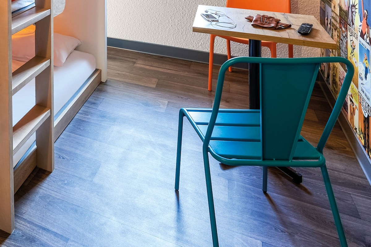 A compact room with a bunk bed, a small table with a chair, and a wall with posters.