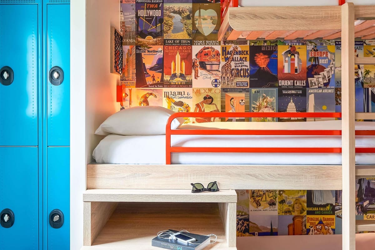 A bunk bed with a wooden frame and a headboard, a small bedside table with a pair of glasses, and a blue cabinet with two drawers.