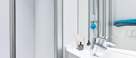Un baño moderno con un lavamanos blanco, un cabezal de ducha de mano y un perchero con toallas dobladas.