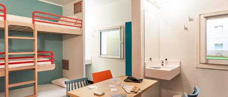 A room with bunk beds, a table with chairs, a window, and a small shelf with toiletries.
